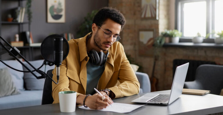 Contabilidade especialista para Infoprodutores: produtor digital trabalhando em home office com microfone, laptop e anotações.